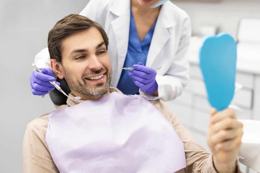 Handsome Smiling Man Patient Looking In Mirror Checking His Teeth